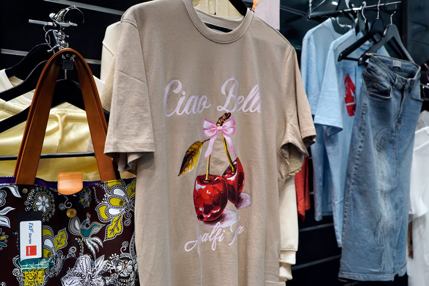 Textile DTF printed cherry design on t-shirt, displayed alongside patterned tote bag on Mimaki TxF Series clothing rail at FESPA 2026